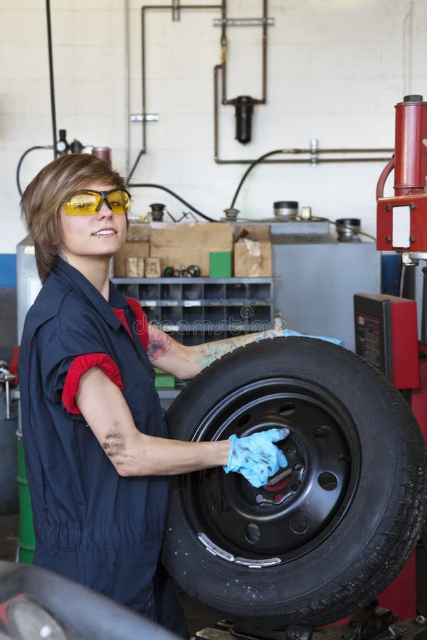 Portrait of a confident young female mechanic carrying tire in vehicle repair shop. Portrait of a confident young female mechanic carrying tire in vehicle repair shop