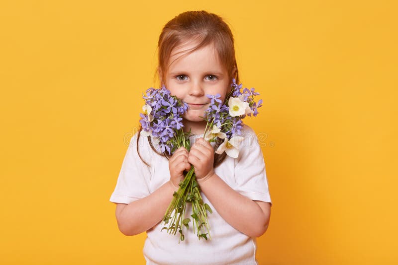 Ståenden av litet barnflickan med buketten av trädgårdblommor som isoleras över gul studiobakgrund, ordnar till för att gratulera arkivfoto Ståenden av litet barnflickan med buketten av trädgårdblommor som isoleras över gul studiobakgrund, ordnar till för att gratulera arkivfoto