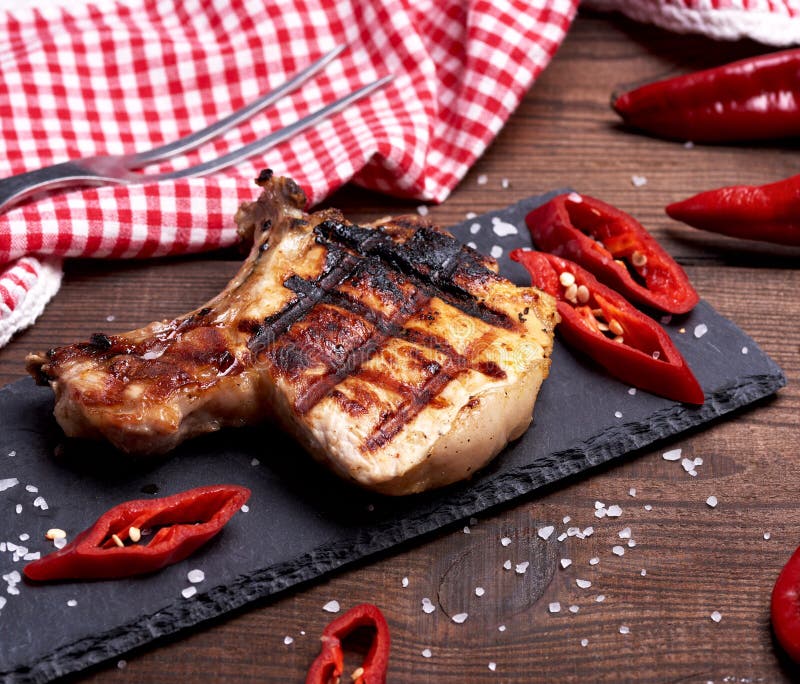 Stück des gebratenen Schweinefilets auf einem Knochen liegt auf einem schwarzen Brett lizenzfreie stockbilder Stück des gebratenen Schweinefilets auf einem Knochen liegt auf einem schwarzen Brett lizenzfreie stockbilder