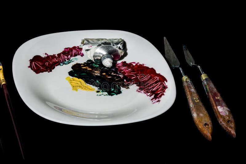 Su un fondo nero è un piatto bianco della porcellana Sul piatto è un tubo di pittura e dei colpi fatti di colore A destra del fotografia stock Su un fondo nero è un piatto bianco della porcellana Sul piatto è un tubo di pittura e dei colpi fatti di colore A destra del fotografia stock