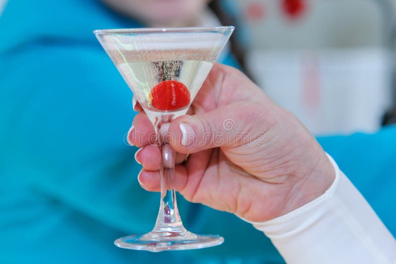 In sua mano un vetro di champagne con una ciliegia dentro fotografia stock libera da diritti In sua mano un vetro di champagne con una ciliegia dentro fotografia stock libera da diritti