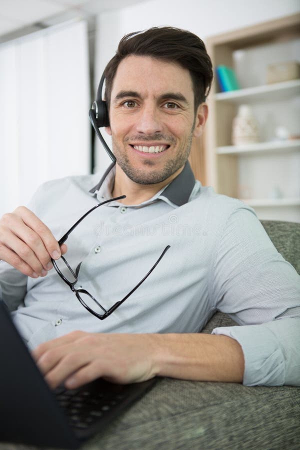 Suave Man Sat on Sofa Using Headset and Laptop Computer Stock Image