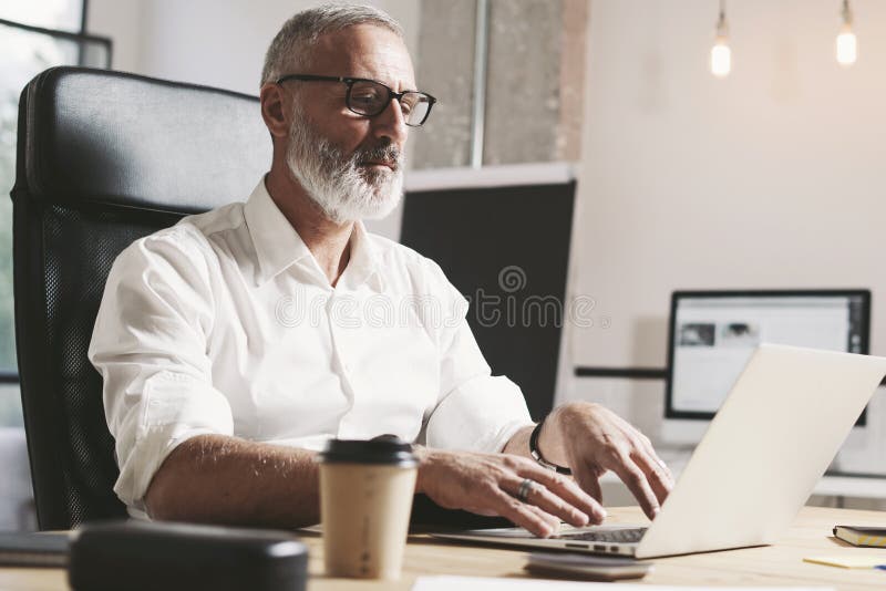 Succes y hombre de negocios adulto confidencial usando el ordenador portátil móvil mientras que trabaja en la tabla de madera en foto de archivo Succes y hombre de negocios adulto confidencial usando el ordenador portátil móvil mientras que trabaja en la tabla de madera en foto de archivo