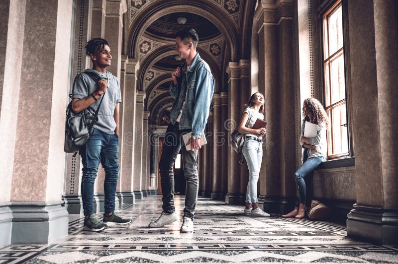 Success and knowledge helps us on the exam. Happy young students standing at the university hall and chatting royalty free stock photo Success and knowledge helps us on the exam. Happy young students standing at the university hall and chatting royalty free stock photo