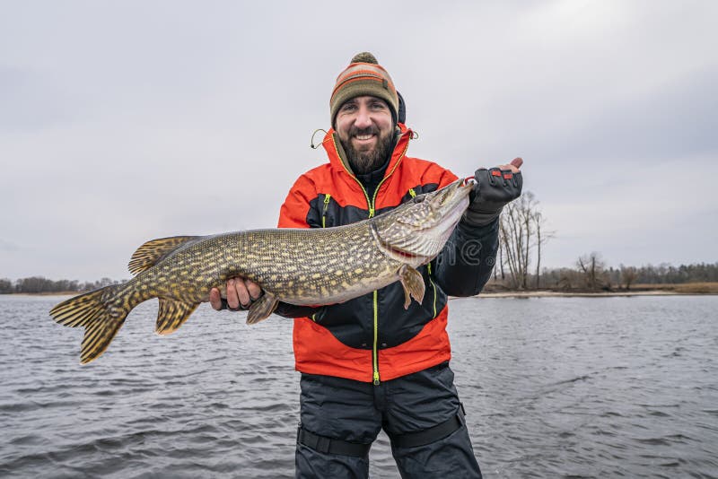 Success pike fishing. Happy fisherman with big fish trophy at boat