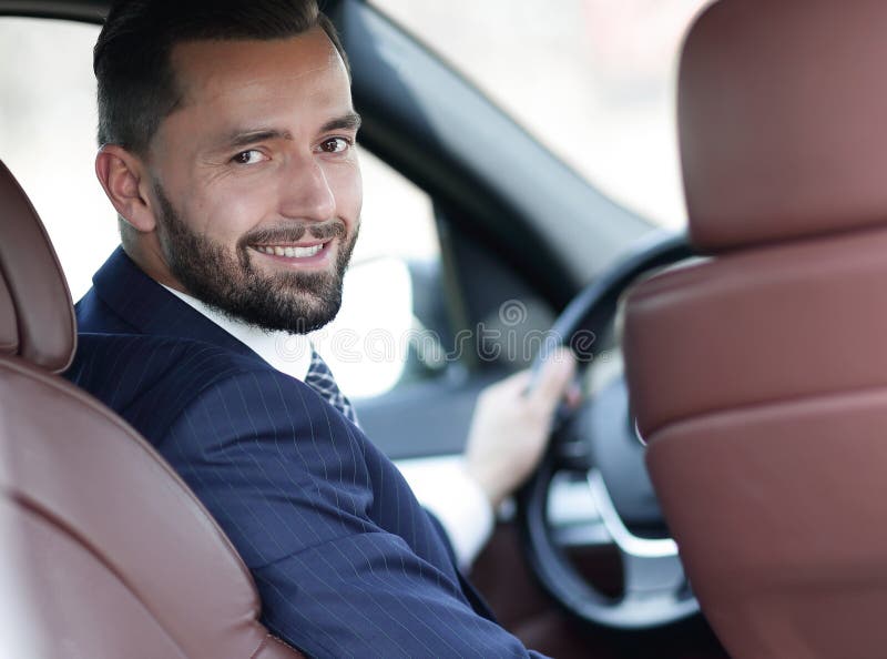 Businessman sitting at the wheel of a car and looking at the cam