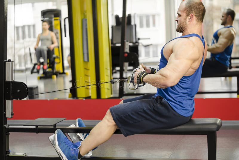 Successful male athlete doing seated cable rows, strong man training in the gym