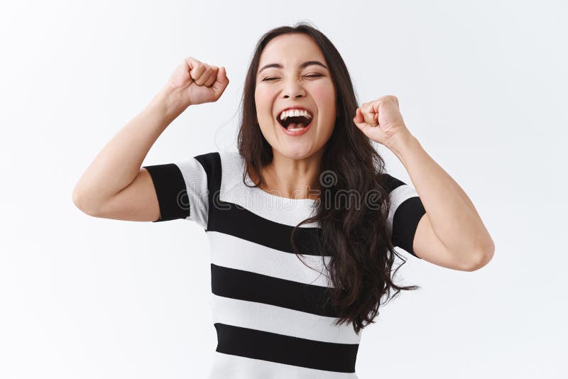 Successful, relieved young happy asian woman in striped t-shirt lifting hands up, fist pump like champion, feel lucky