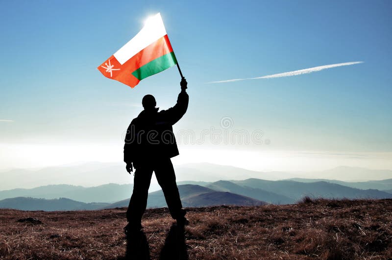 Successful silhouette man winner waving Oman flag on top of the mountain royalty free stock images