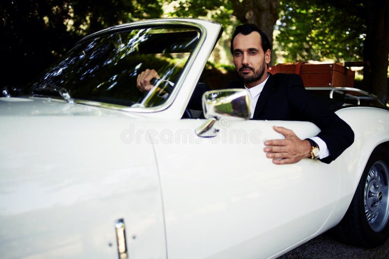 Successful and wealthy businessman sitting behind the wheel of his luxury cabriolet car on countryside road