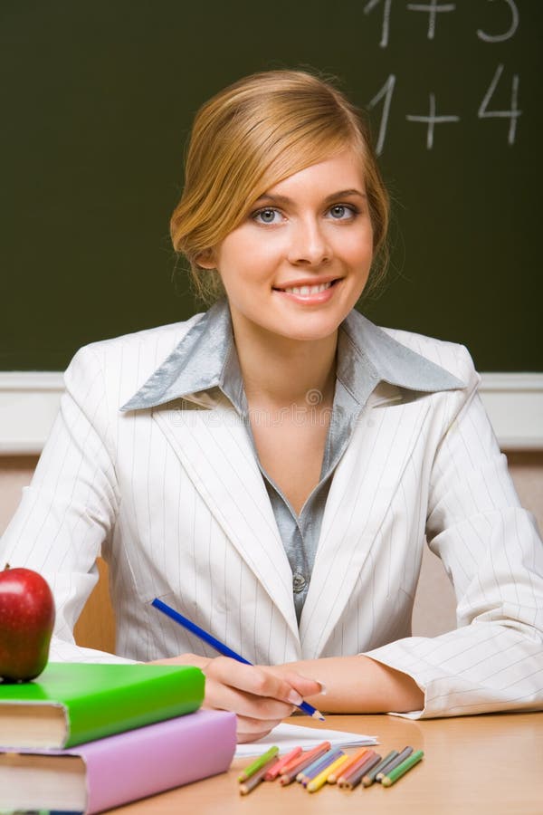 Portrait of young teacher checking up copybook with books near by and looking at camera with smile. Portrait of young teacher checking up copybook with books near by and looking at camera with smile