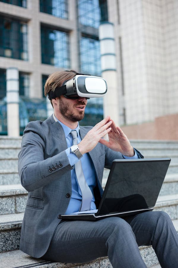 Successful young businessman using virtual reality simulator goggles and making hand gestures, working on a laptop in front of an royalty free stock photography Successful young businessman using virtual reality simulator goggles and making hand gestures, working on a laptop in front of an royalty free stock photography