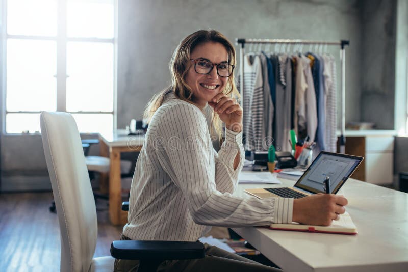 Smiling young woman taking note of orders from customers. Dropshipping business owner working in her office. Smiling young woman taking note of orders from customers. Dropshipping business owner working in her office