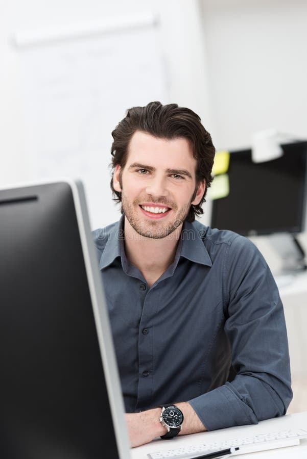 Successful confident businessman with a warm friendly smile sitting at his desk in the office looking at the camera. Successful confident businessman with a warm friendly smile sitting at his desk in the office looking at the camera