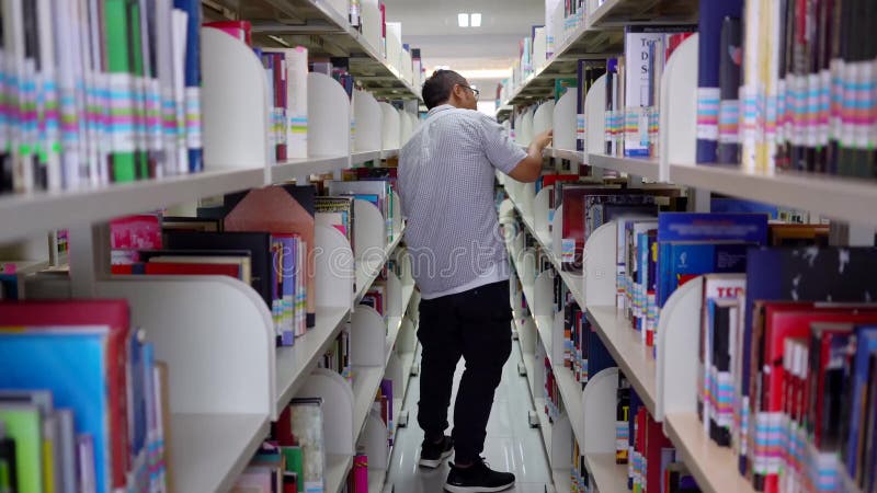 Suchendes Buch des männlichen asiatischen Studenten in der Bibliothek