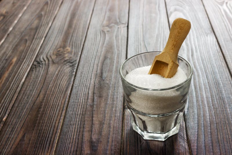Sucre granulé de blanc dans la tasse blanche avec la cuillère en bois sur le fond en bois image libre de droits Sucre granulé de blanc dans la tasse blanche avec la cuillère en bois sur le fond en bois image libre de droits