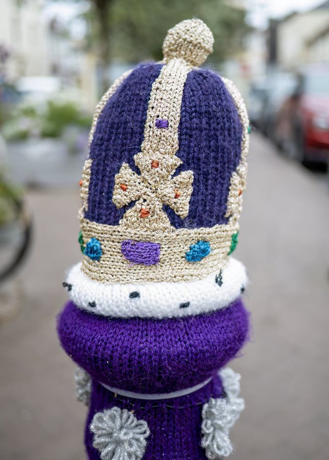 SOUTH MOLTON, DEVON, ENGLAND - AUGUST 2 2022: Post in street with knitted crown on top, yarn bombing. Royal purple. SOUTH MOLTON, DEVON, ENGLAND - AUGUST 2 2022: Post in street with knitted crown on top, yarn bombing. Royal purple.