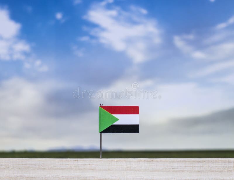 Sudan flag with vast meadow and blue sky behind it. royalty free stock photography