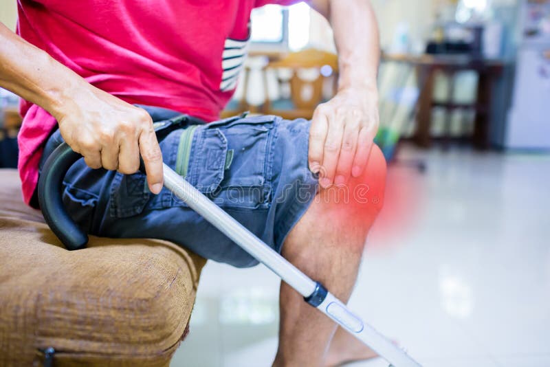 Sufrimiento del hombre del dolor de la rodilla y sentada del bastón en el sofá fotografía de archivo libre de regalías Sufrimiento del hombre del dolor de la rodilla y sentada del bastón en el sofá fotografía de archivo libre de regalías