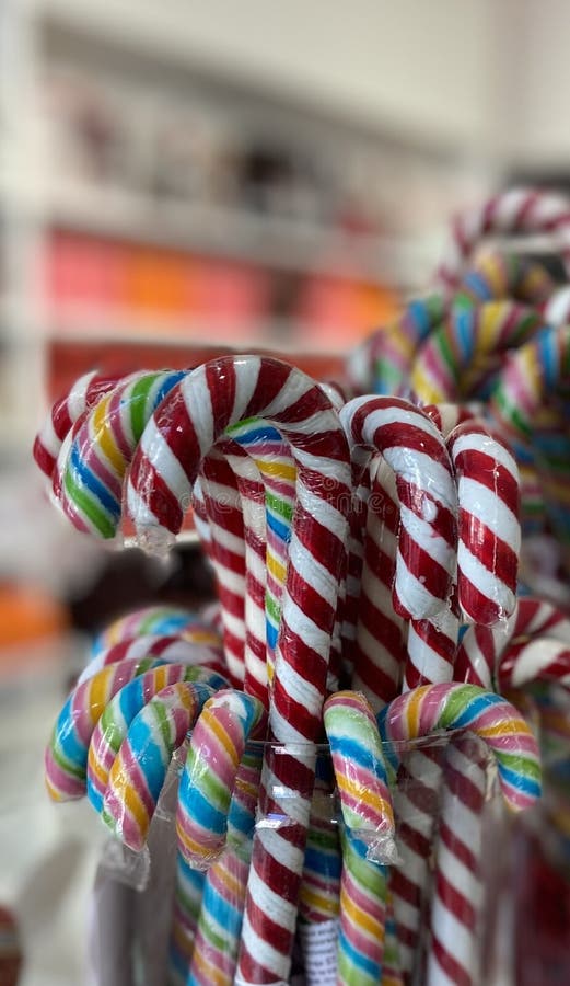 Sugar canes in candy store. A candy cane is a cane-shaped stick candy often associated with Christmastide, as well as Saint Nicholas Day. It is traditionally white with red stripes and flavored with peppermint, but they also come in a variety of other flavors and colors