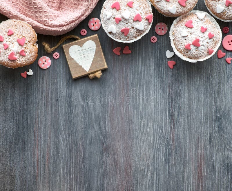 Sugar-sprinkled muffins with pink and white fondant icing hearts, background
