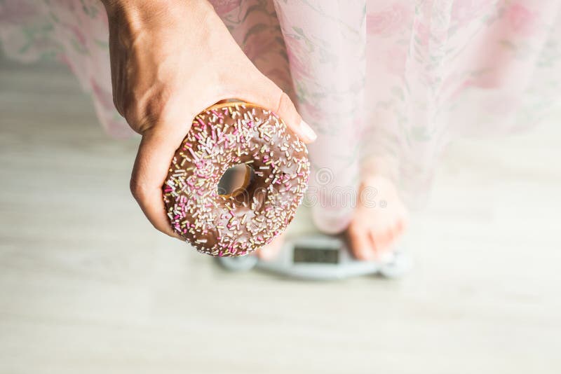 Suivez un régime le concept Plan rapproché des pieds du ` s de femme sur la balance avec le beignet Concept des bonbons, de la no photo libre de droits Suivez un régime le concept Plan rapproché des pieds du ` s de femme sur la balance avec le beignet Concept des bonbons, de la no photo libre de droits