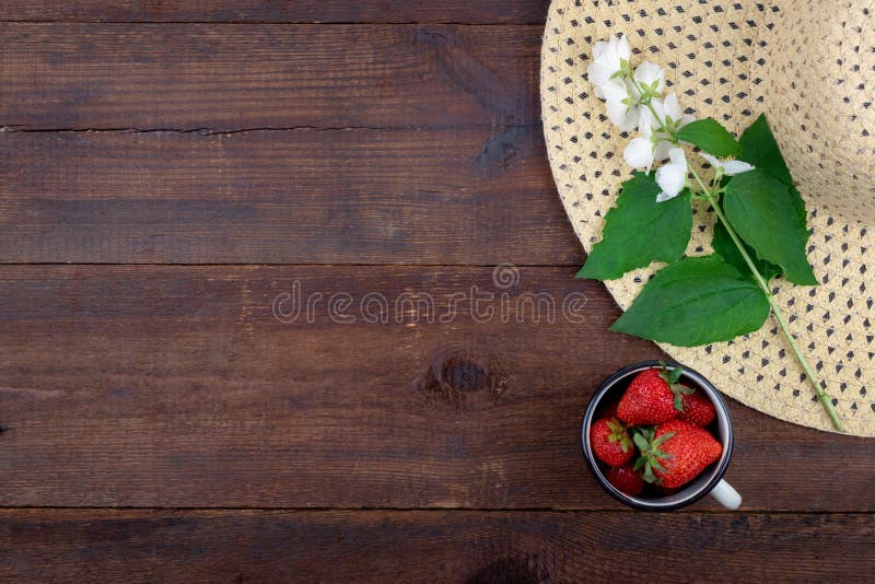 Summer background with straw hat, strawberries in cup and white flowers with green leaves on wooden background. Summer berry royalty free stock image Summer background with straw hat, strawberries in cup and white flowers with green leaves on wooden background. Summer berry royalty free stock image