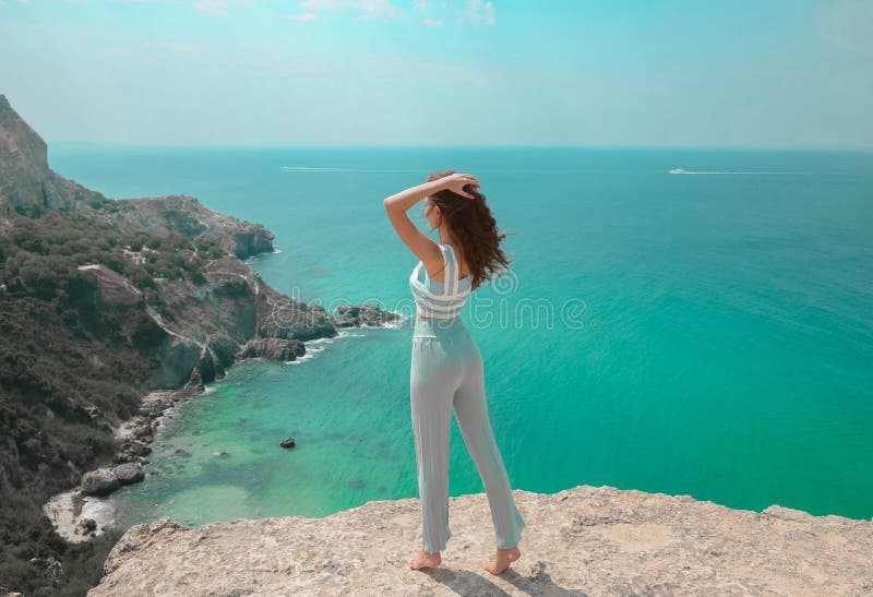 Summer beach fashion woman outfit. Beautiful traveller girl having fun on cliff mountains enjoying lagoon bay. Summertime