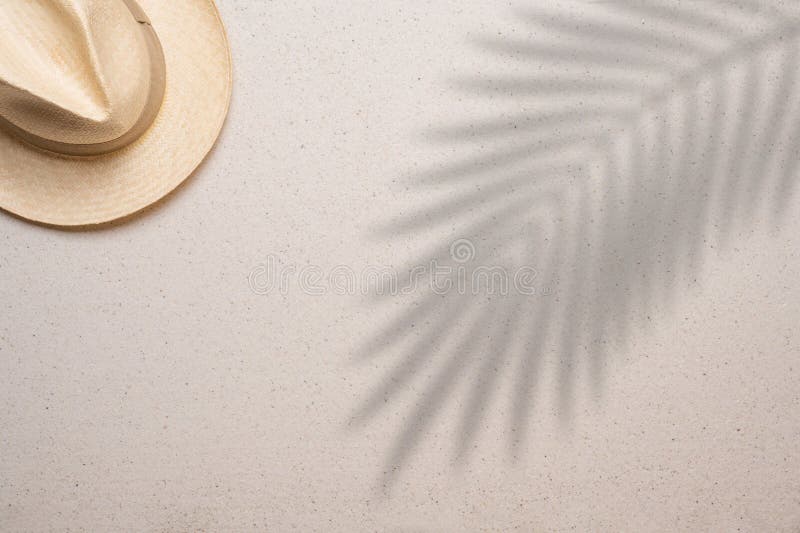 Straw hat in the upper left corner on a fine sandy background and with a palm leaf shade in the right side