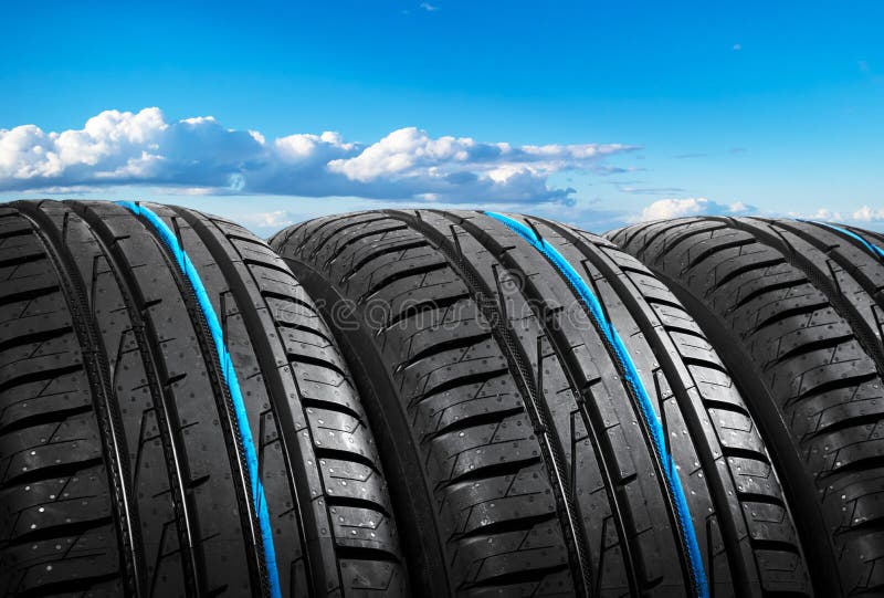 Summer car tires on over blue sky with clouds. Tire stack background. Car tyre protector close up. Black rubber tire. Brand new