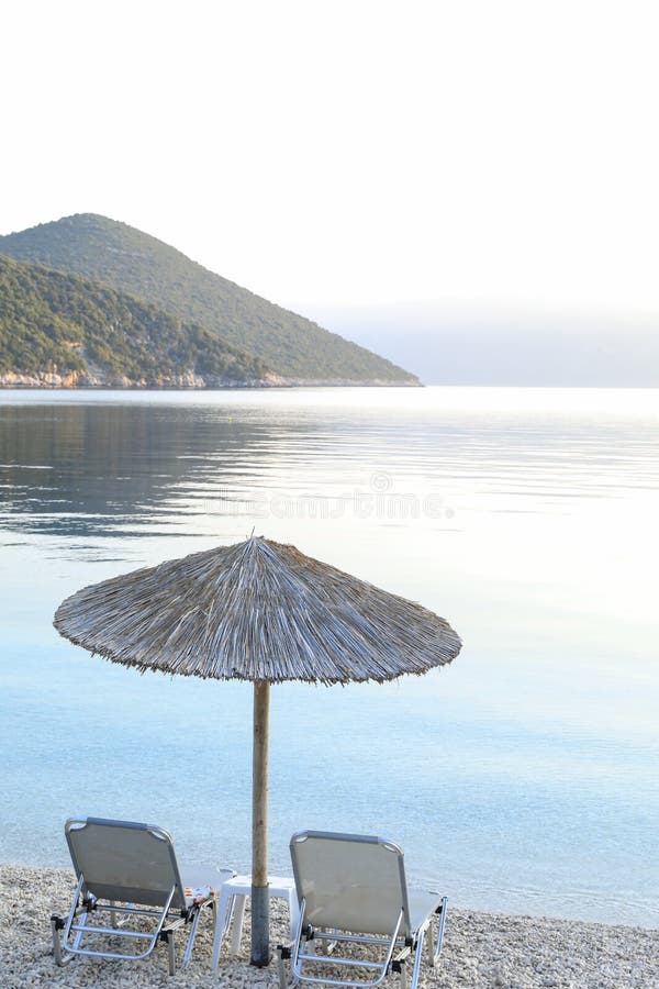 Summer early morning straw umbrella and two sunbeds on a beautiful Antisamos beach of Kefalonia island, Ionian sea, Greece stock images Summer early morning straw umbrella and two sunbeds on a beautiful Antisamos beach of Kefalonia island, Ionian sea, Greece stock images