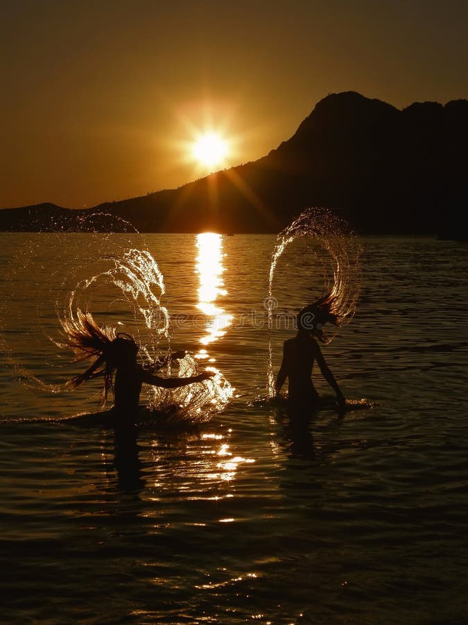 Two active young girls (best friends - sisters) have a fun in water (doing a water hair splash) at golden sunset in summer holiday at Adriatic sea (Croatia-Dalmatia). Vertical color photo. Two active young girls (best friends - sisters) have a fun in water (doing a water hair splash) at golden sunset in summer holiday at Adriatic sea (Croatia-Dalmatia). Vertical color photo.