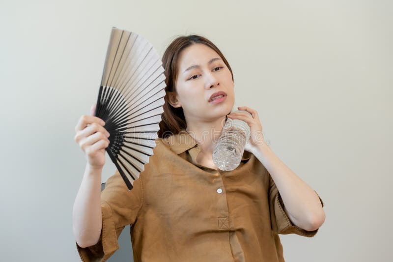 Summer heat stroke, hot weather, tired asian young woman sweaty and thirsty, refreshing with hand in blowing, wave fan to