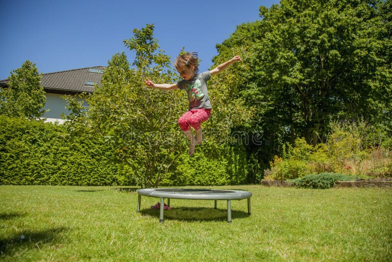 Summer holiday concept. Little cute child girl having fun outdoors and she jumping on a trampoline