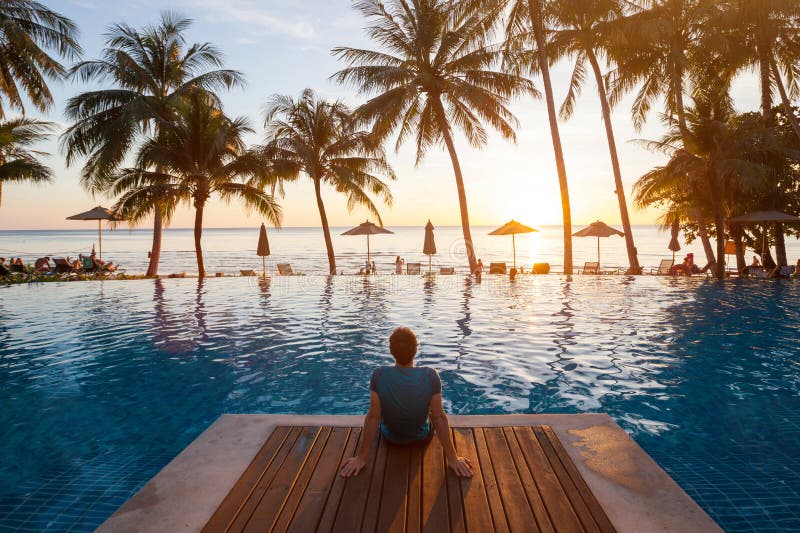 Luxury beach hotel, tourist relaxing near luxurious swimming pool at sunset, vacation on tropical island