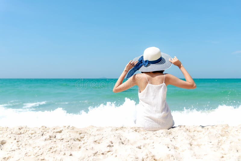 Summer Holiday. Lifestyle woman white dress wearing fashion summer trips sitting on the sandy ocean beach. Happy woman enjoy and r