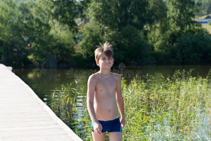 Happy boy 11 years old goes swimming on a wooden pier, on the background of the shore and the lake on a summer sunny day royalty free stock photos Happy boy 11 years old goes swimming on a wooden pier, on the background of the shore and the lake on a summer sunny day royalty free stock photos