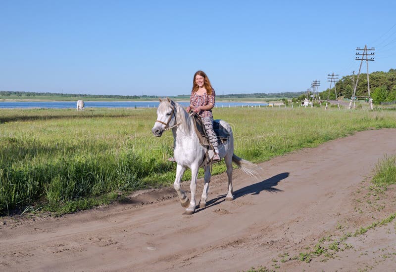 Happy girl riding on horseback, on a rural road, against the backdrop of a lake. royalty free stock photography Happy girl riding on horseback, on a rural road, against the backdrop of a lake. royalty free stock photography