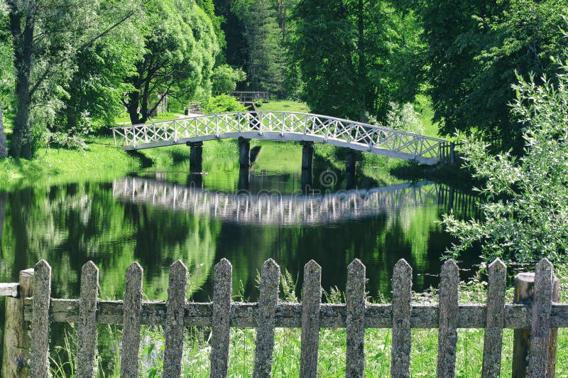 Summer landscape with lush greenery and white wooden bridge reflected in the water surface of the pond Mikhailovskoye village, Russia