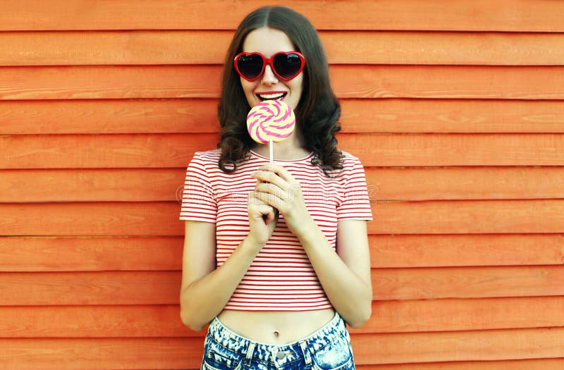 Summer portrait of happy smiling young woman with lollipop in amusement park on wooden wall