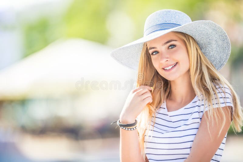 Summer portrait of young beautiful woman in hat sitting on bench in park