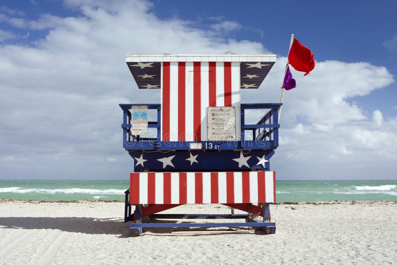 Summer scene with a lifeguard house in Miami Beach, Florida in the colors of the American flag with blue sky and ocean in the background. Back centered view.