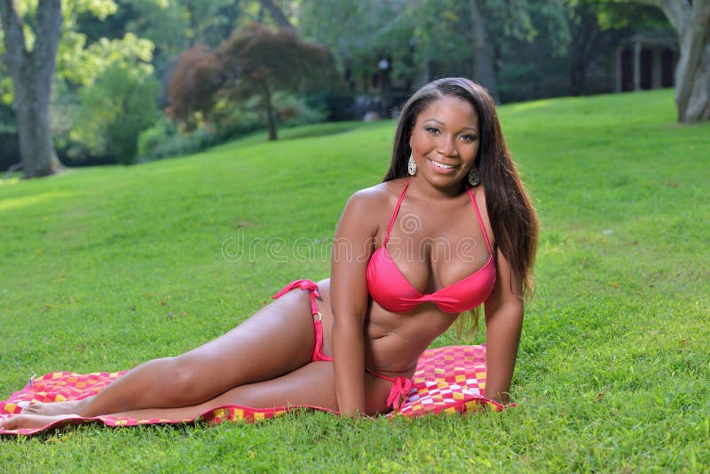 Beautiful African-American woman in red bikini sits on beach towel in grass - summer. Beautiful African-American woman in red bikini sits on beach towel in grass - summer