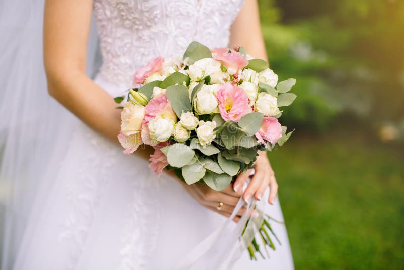 Summer shot of a wedding bouquet of roses pink and white colors in the hands of the bride on the street among the