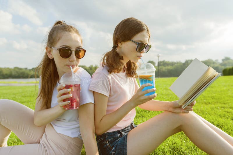 Summer sunny day, two girlfriends teenagers sit on green lawn, drink cocktails, talk, read book, laugh, have fun. stock image Summer sunny day, two girlfriends teenagers sit on green lawn, drink cocktails, talk, read book, laugh, have fun. stock image