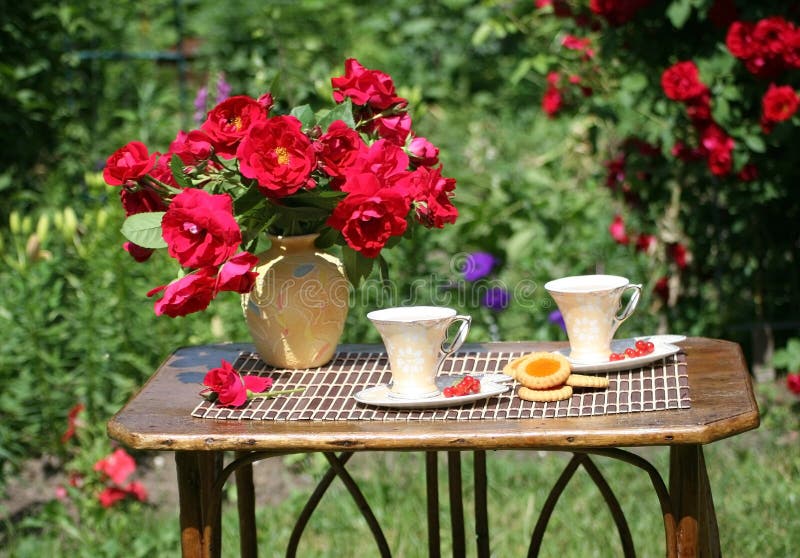 In un giardino c'è un piccolo tavolo con un mazzo di rose e una tazza di tè.