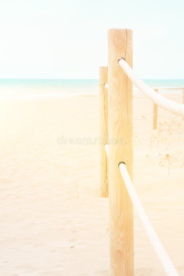 Summer travel vacation concept. White pinkish beach sand turquoise ocean blue sky. Tranquil idyllic scene. Rope railing