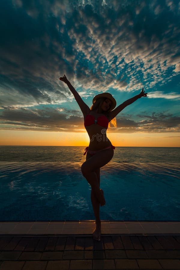 Summer Vacation. Silhouette of beauty dancing woman on sunset near the pool with ocean view.