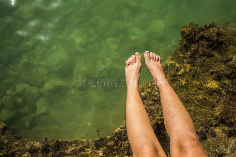 Summer vacation holidays concept of female feet on rock stones above sea shore water vivid water surface, copy space stock photos