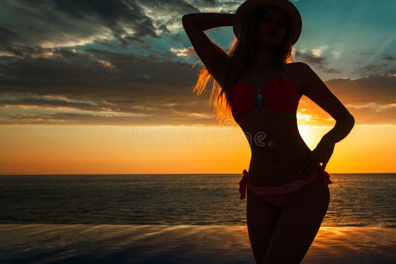 Summer Vacation. Silhouette of beauty dancing woman on sunset near the pool with ocean view.